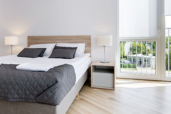 Bright modern bedroom with queen bed, dark bedding, wood headboard, nightstands with lamps, and glass doors opening to patio.