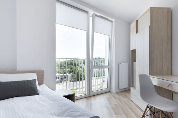 Modern bedroom with bed, glass balcony doors, desk, and wardrobe with light wood and white finishes