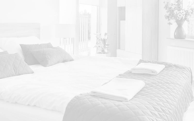 Bright modern bedroom with white bedding, gray pillows, large windows, and minimalist furnishings