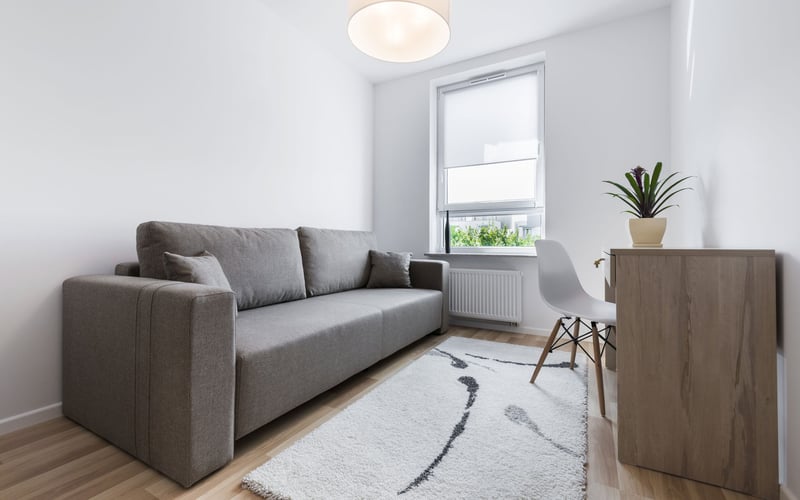Bright living room with gray sofa, wooden side table with potted plant, modern chair, and window with roller shade